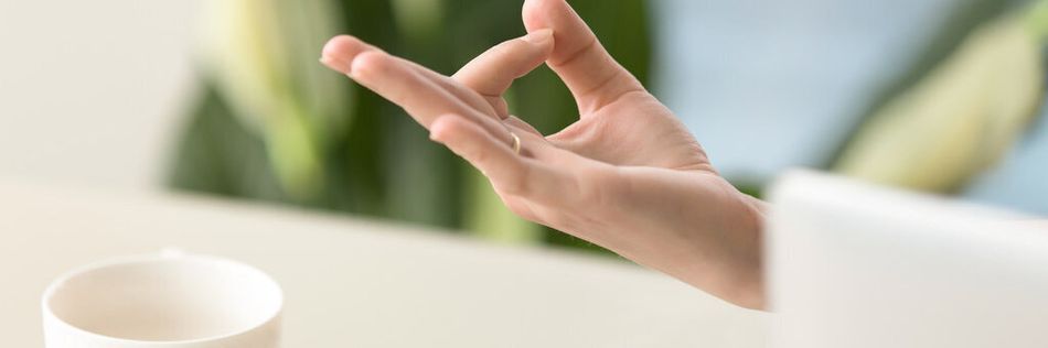 Teetasse auf einem Tisch und eine Hand in Yoga-Position im Vordergrund